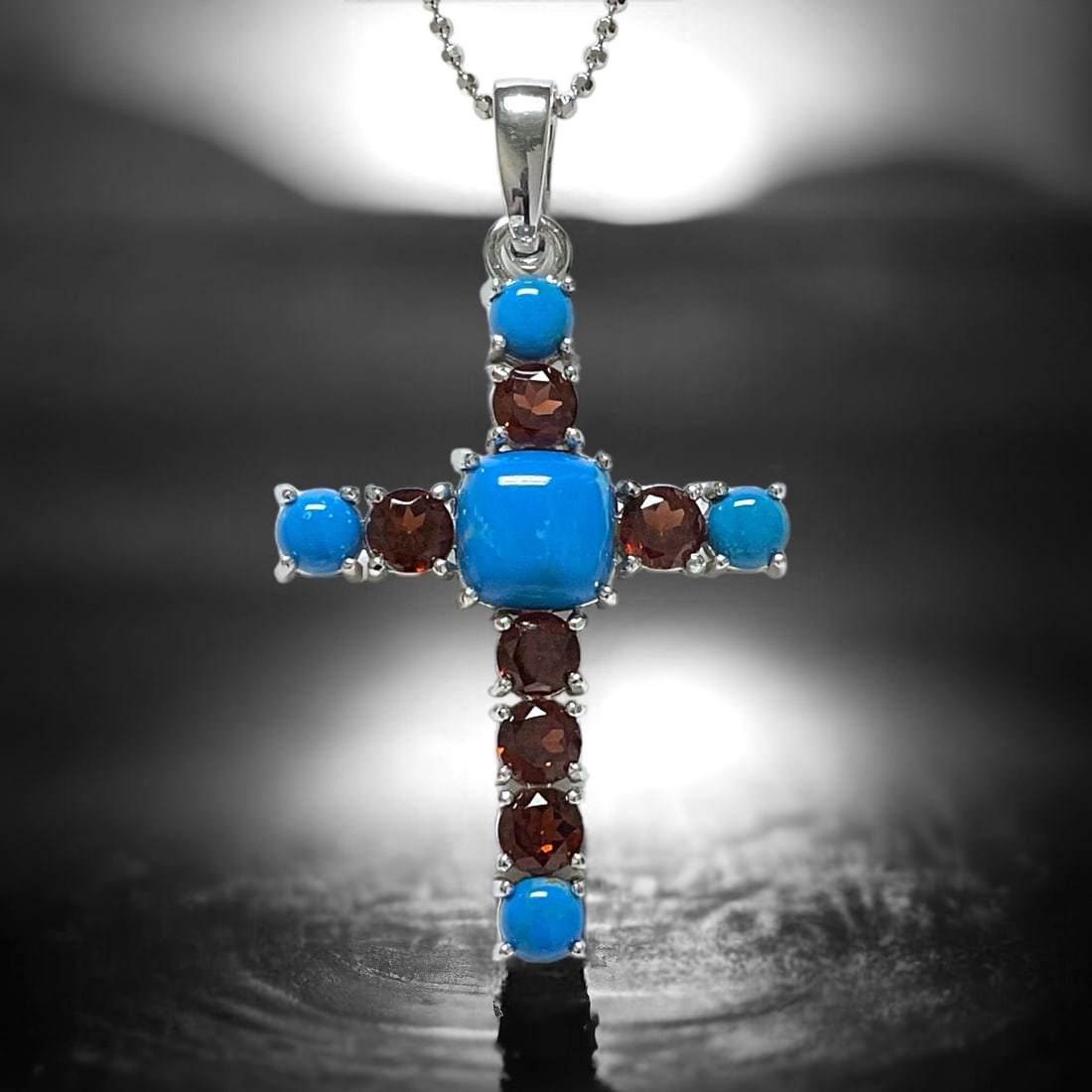 Spiritual Sterling Silver Cross Pendant with Blue Ceruleite & Garnet: Stabilized Ceruleite: One cushion shaped 9.5 mm cabochon and four round 5 mm cabochons Garnet: Six round modified-brilliant cut 5 mm Product Details Item: Pendant Metal: Sterling Silver Gemstone: Ceru