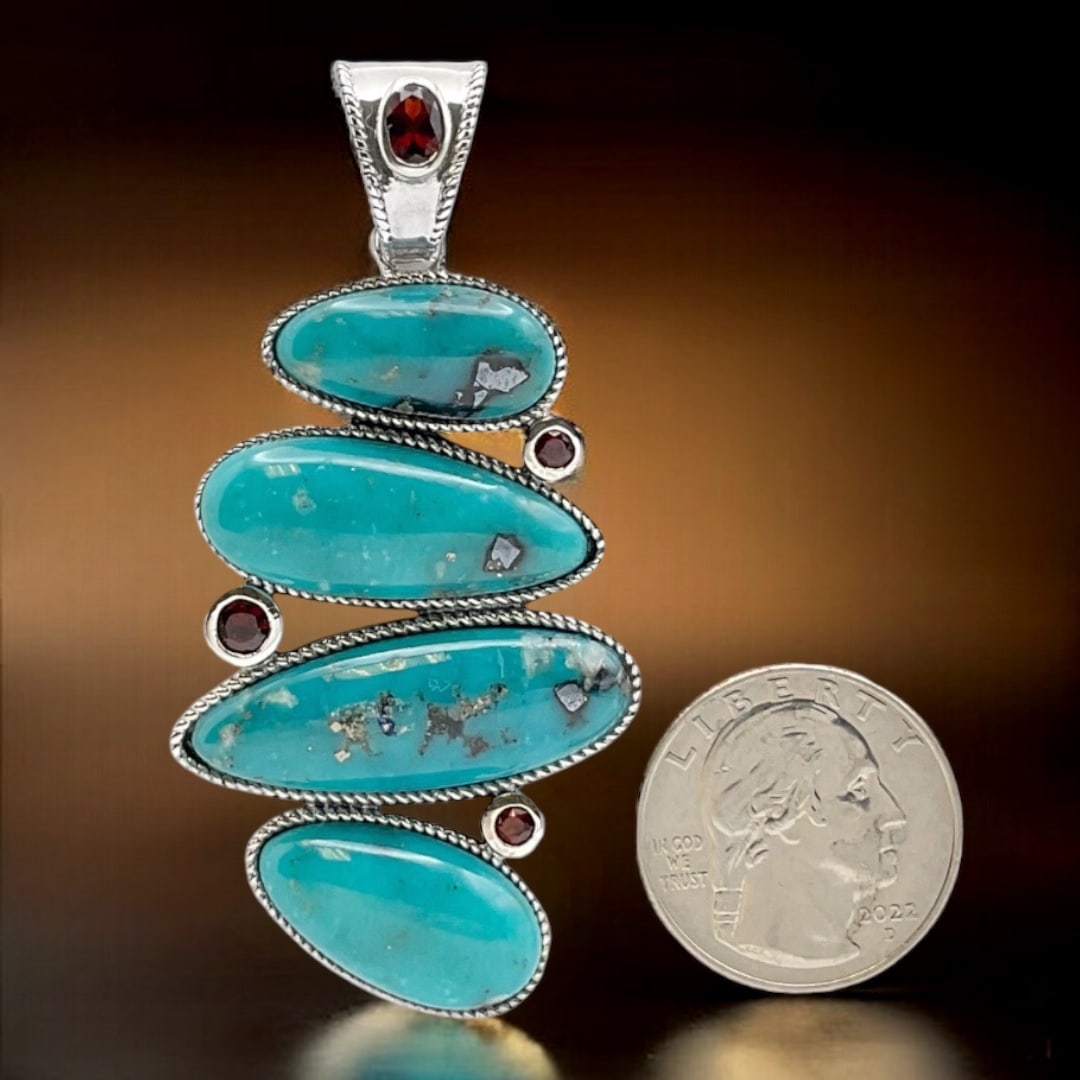Campo Frio Turquoise Pendant combined with Garnet and crafted in Sterling Silver: Product Details Item: Pendant Metal: Sterling Silver Gemstone: Campo Frio Turquoise & Garnet Approximate Measurements: 69.6X34.3 mm Ring Size: Not Applicable Chain Length: Not Applicable