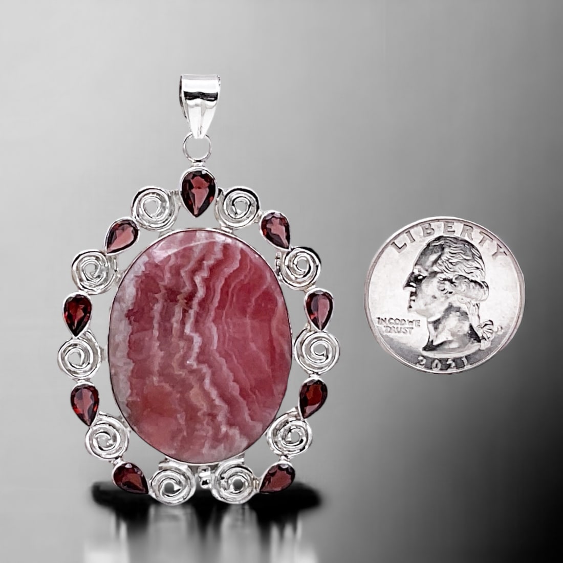 Oval Rhodochrosite Gemstone Pendant set in Sterling Silver with Marquise cut Garnet: Product Details Item: Pendant Metal: Sterling Silver Gemstone: Rhodochrosite & Garnet Approximate Measurements: 63.2 mm X 41.7 mm Ring Size: Not Applicable Chain Length: Not Applicable