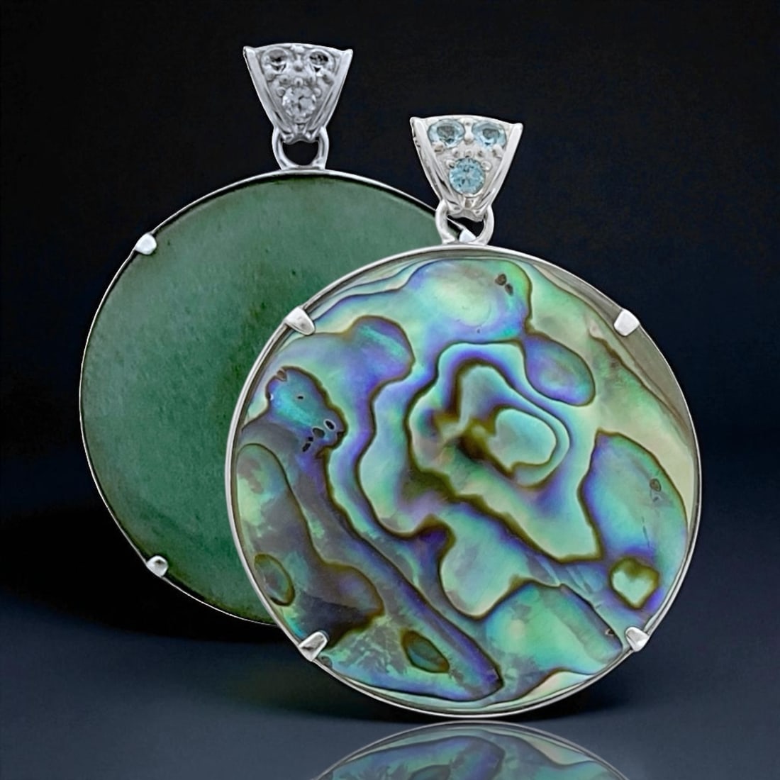 Reversible Sterling Silver Pendant with Green Adventurine and Abalone: 40 mm Round Centerstones: Abalone & Green Adventurine 3 mm Blue Topaz & 3 mm White Topaz Product Details Item: Pendant Metal: Sterling Silver Gemstone: Adventurine, Abalone, Swiss Blue Topaz, White To