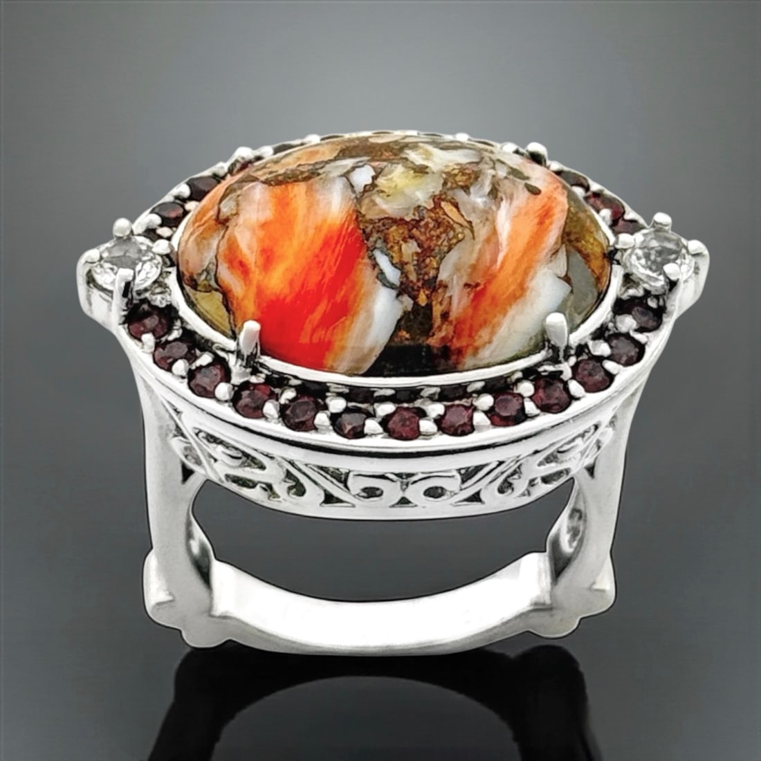 Vibrant Orange Spiney Oyster & Garnet East-West Halo Ring - Size 7: Product Details Item: Ring Metal: Sterling Silver Gemstone: Orange Spiney Oyster & Garnet Approximate Measurements: Width: 19.2 mm Ring Size: 7 Chain Length: Not Applicable Chain Met