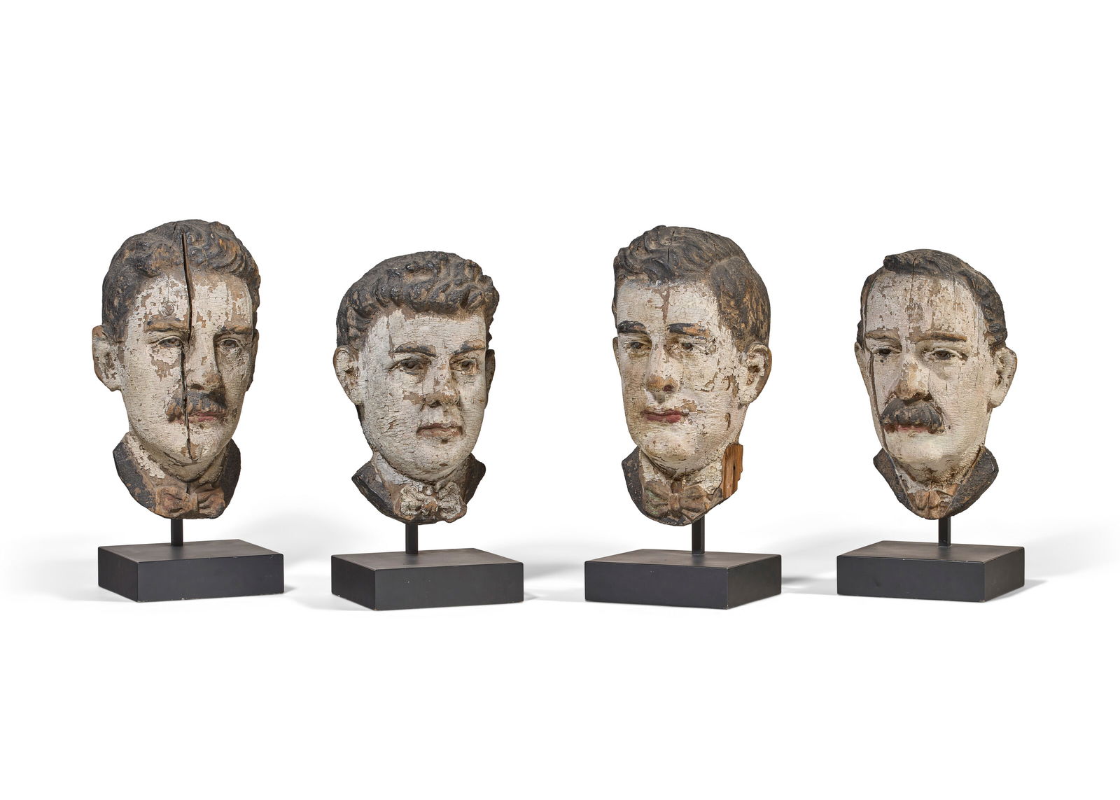 FOUR CARVED PINE AND POLYCHROME PAINT-DECORATED HEADS AMERICAN, LATE 19TH CENTURY: FOUR CARVED PINE AND POLYCHROME PAINT-DECORATED HEADS AMERICAN, LATE 19TH CENTURY Details The back of each head numbered I, II, III, IIII The larger two: 18 1/2 in. (47 cm.) high (without stands) Prov