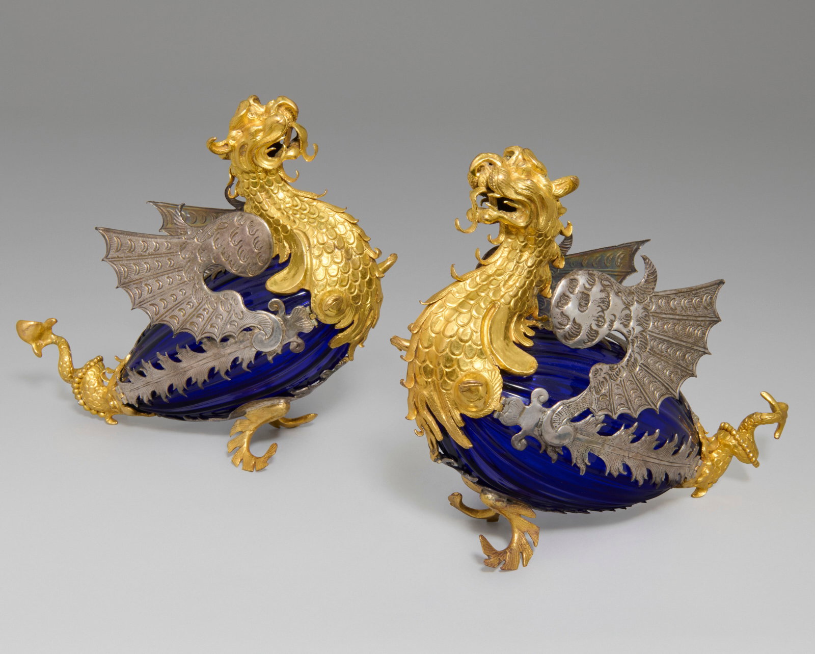 A PAIR OF SILVER AND GILT-COPPER MOUNTED BLUE GLASS DRAGONS ITALIAN, PROBABLY FLORENCE, CIRCA 1615: Details A PAIR OF SILVER AND GILT-COPPER MOUNTED BLUE GLASS DRAGONS ITALIAN, PROBABLY FLORENCE, CIRCA 1615 the blue glass bodies possibly original, with some restoration and replacements to the silver