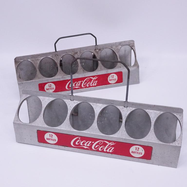 Aluminum 12 Bottle Carriers: Two aluminum 12 bottle carriers. Circa 1950's. Stamped "Property of Coca-Cola Bottling Plant." Retractable metal handles. 5.25" x 16.25" ~ 7.25" retracted. Some wear and damage.