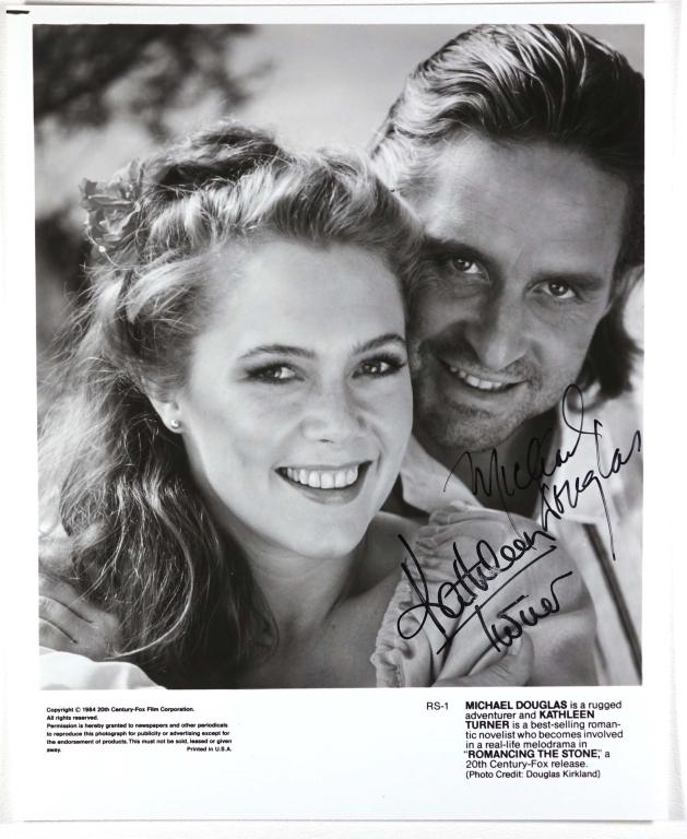 Autographs: Kathleen Turner & Michael Douglas: Kathleen Turner & Michael Douglas DOUBLE SIGNED 7-15/16 x 9-13/16" black & white 20th Century Fox promo photo for the 1984 romantic -action-adventure-comedy "Romancing the Stone". ** Lot 14 makes the