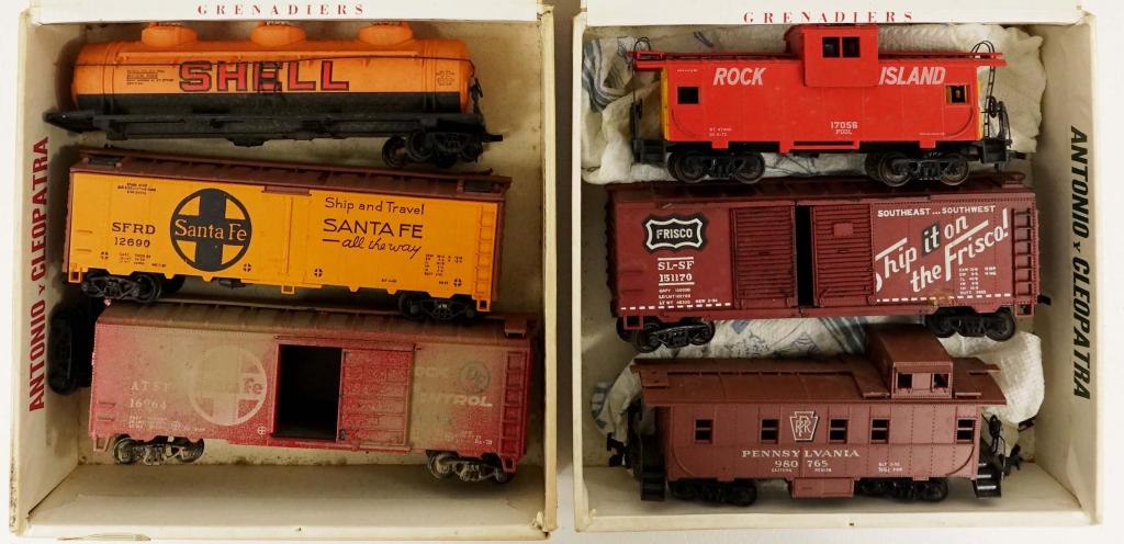 33 Assorted Vintage Train Cars: HO scale (?). Have been stored in cigar cases: each of the 11 cigar cases has 3 train cars. Some are damaged/small pieces have fell off due to storage. Smells smoky.