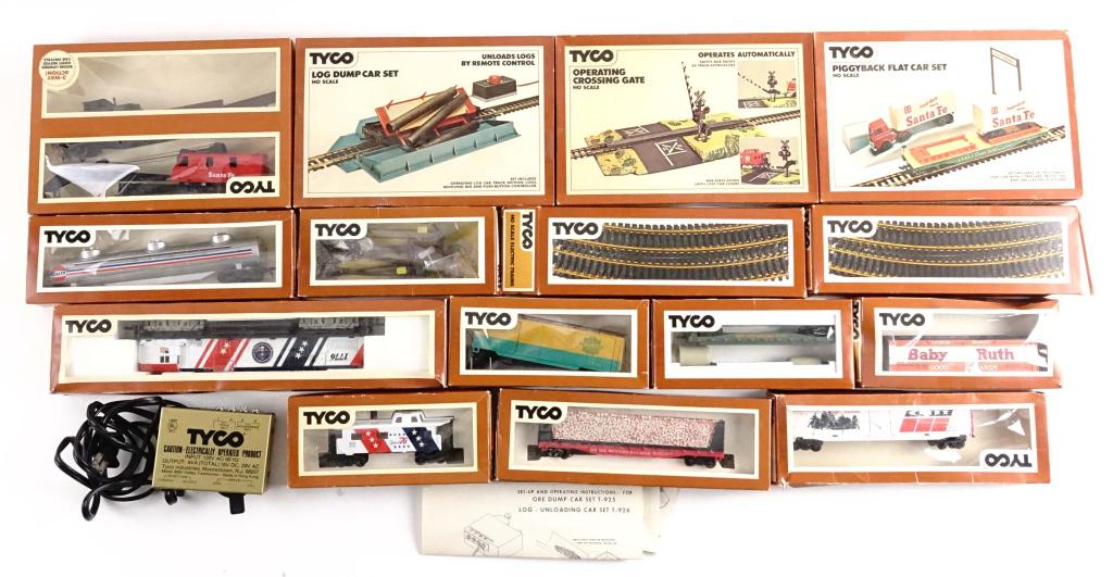 HO Tyco Traincars and Accessories: 9 Traincars; 1 Piggyback Flat Car Set; 1 Operating Crossing Gate; 1 Log Dump Car Set; 1 United States Locomotive; 1 TYCO Powerpak; 2 Boxes of HO Tracks.