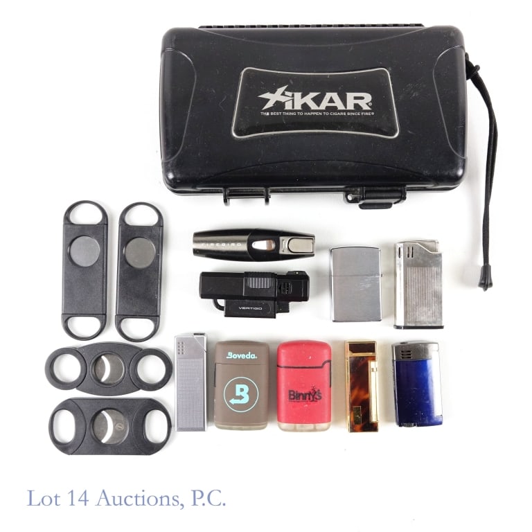 Cigar Cutters, Lighters, Case, Accessories: Xicar Hand-held humidor. One latch is missing. Approximately 8.5" x 4.75" x 2". ** 4 cigar cutters (2 are one-blade, 2 are two-blade). ** 9 lighters. Brands include: Firebiard, Vertigo, Boveda, Braun,