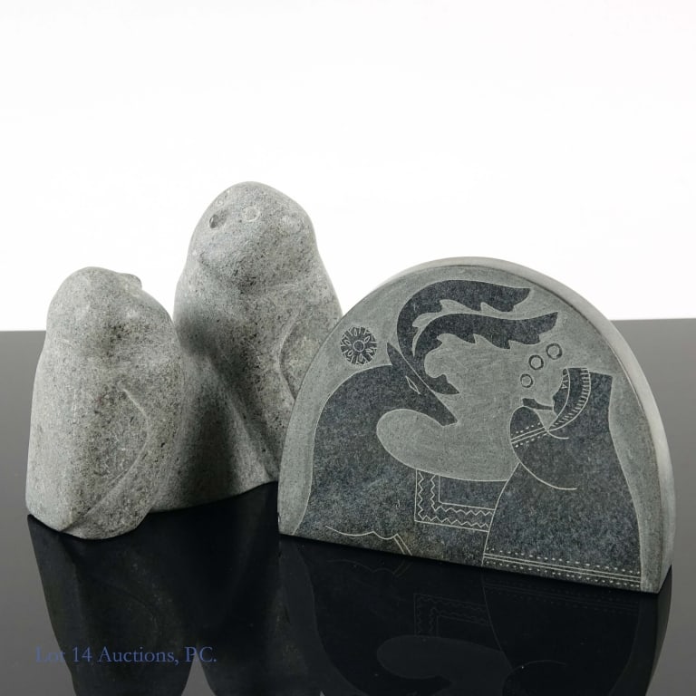 Two Stone Carvings: Two Inuit or Inuit inspired stone carvings. The first depicts a reindeer beside a person smoking a pipe. On the underside is a sticker reading "Made in USSR". The piece measures approximately 4.25 x 3