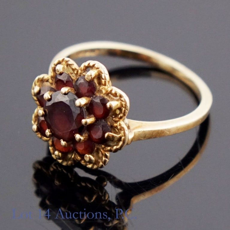 10k Yellow Gold & Garnet Ring: Size 6.5 yellow gold ring marked "10KP" decorated with one large dark red stone and eight smaller of the same stone, probably garnet. Weighs approximately 2.61g or 0.08 troy oz.