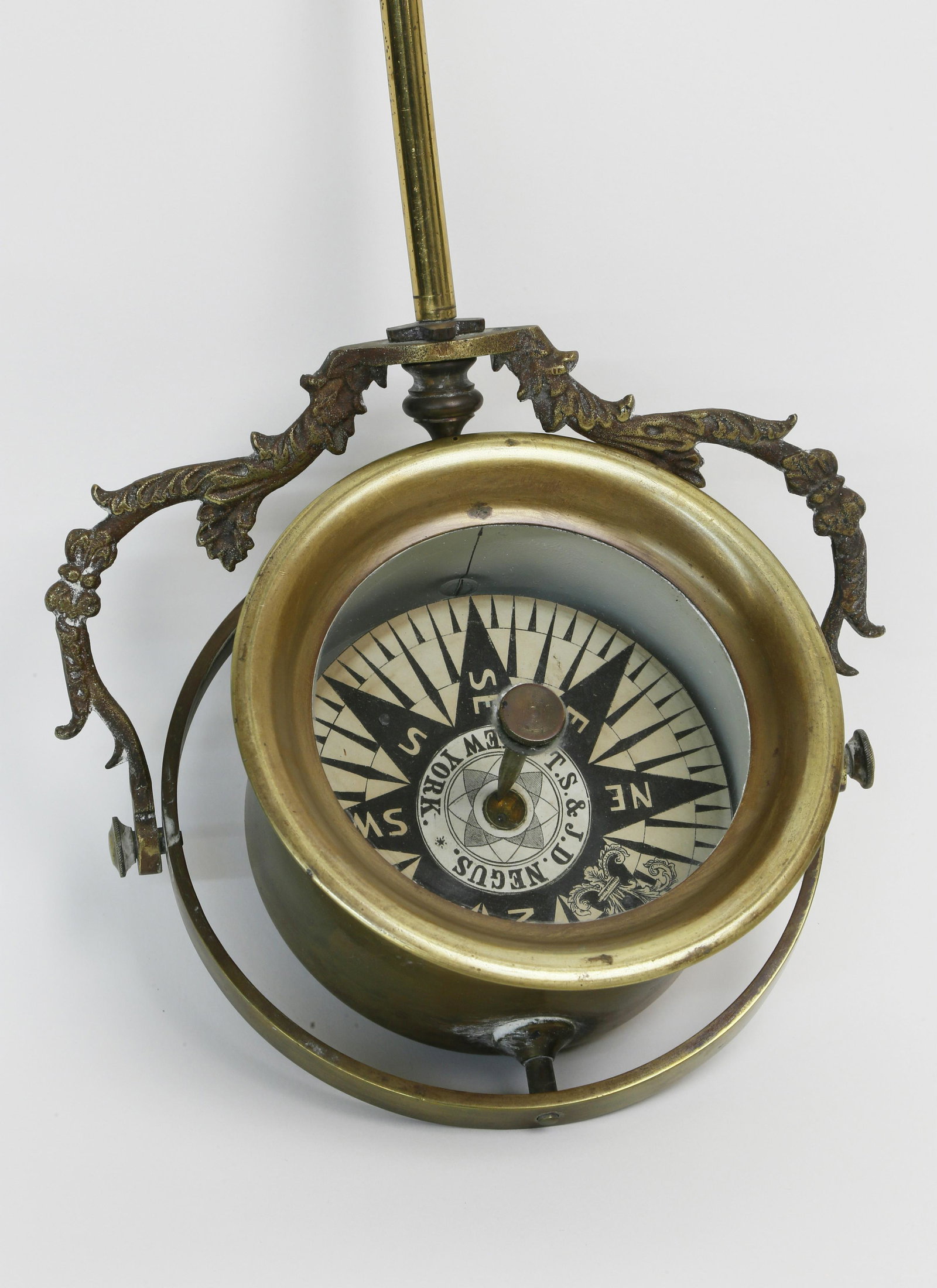 TS & JD Negus, Tell-tale Compass, NY, 19th Century: T.S. & J.D. Negus, Tell-tale Compass, New York, 19th Century, cylindrical brass bowl 5 ¼ in. diameter, gimbal ring and leaf molded brass support, reverse reading compass card. Diameter 5 ¼ in.