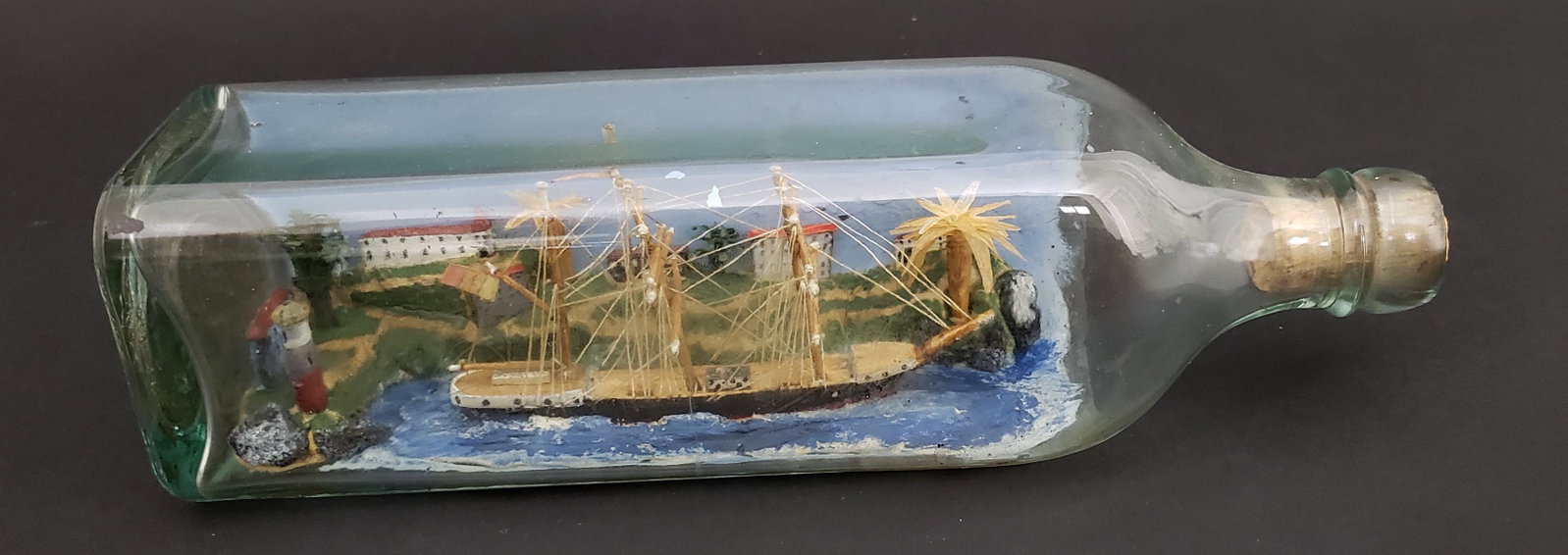 Vintage Folk Art Ship In a Bottle: Vintage Folk Art Ship In a Bottle, with lighthouse and harbor decoration in a village. Height 2.75 in. Width 10.25 in. Depth 2.75 in. Dimensions Height 2.75 in. Width 10.25 in. Depth 2.75 in.