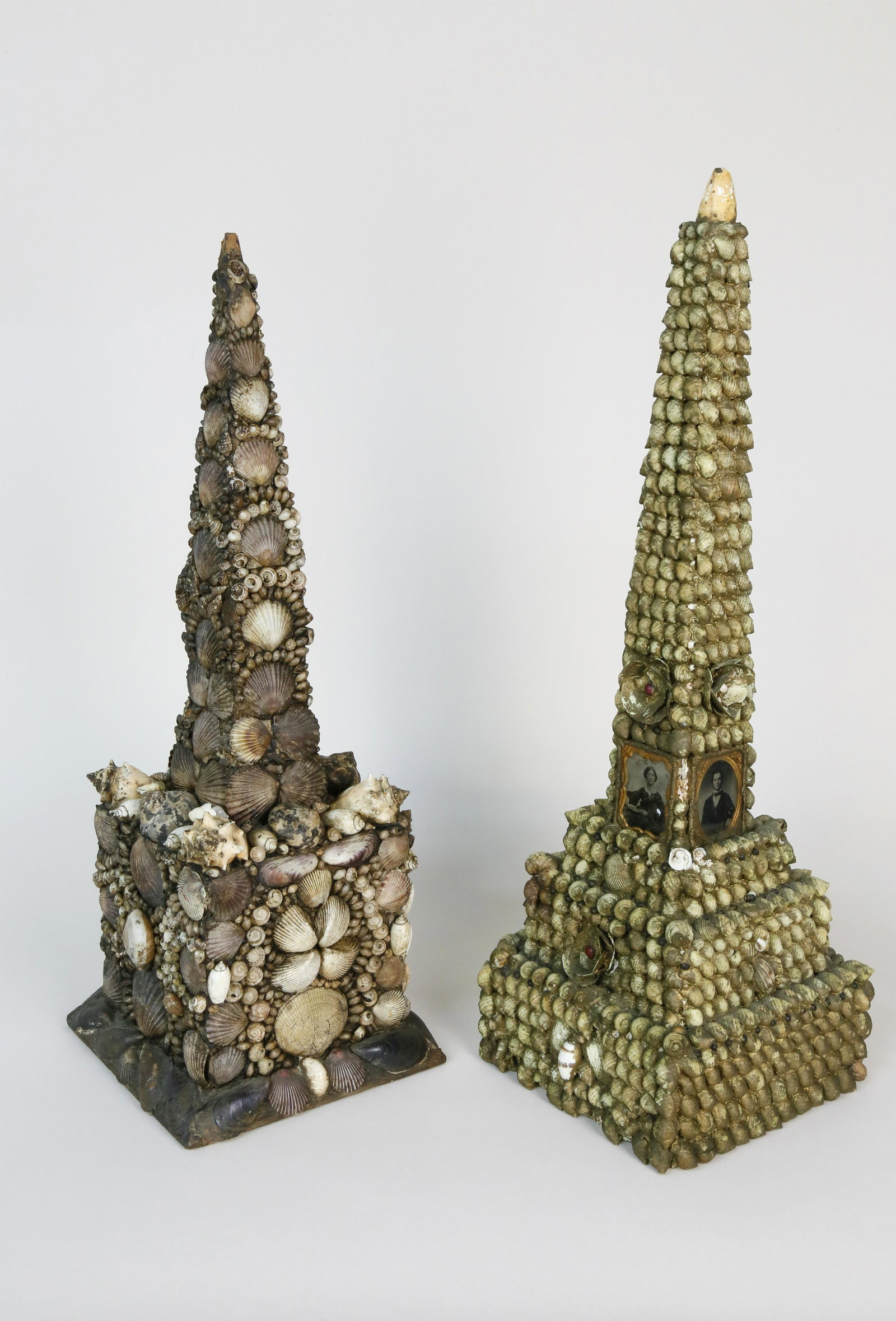 Two American Seashell Encrusted Obelisks, 19th c.: Two American Seashell Encrusted Obelisks, late 19th Century, one applied with three daguerreotype family portraits on stepped base; the other with drawer in plinth. Heights 23 ¾ in. and 22 &fra