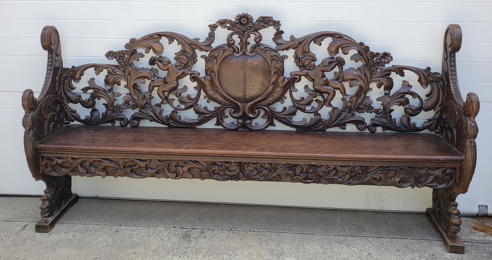 Antique English Oak Rococo Revival Hall Bench, 19th century: Antique English Oak Rococo Revival Hall Bench, 19th century, ornately carved with scrolling acanthus leaf crest with a central medallion backing flanked by cherubs, raised by figural supports. Height
