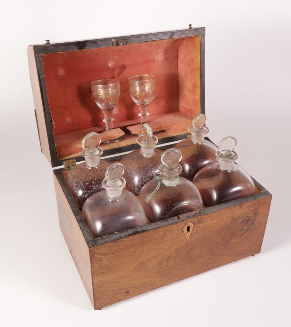 Mahogany Decanter Case, 19th Century: Mahogany Decanter Case, 19th Century, curved-front hinge cover opens to six stopped glass bottles and a pair of stem wines; gilt embellishments Height 8.75 in. Length 10.5 in. Depth 7 in.