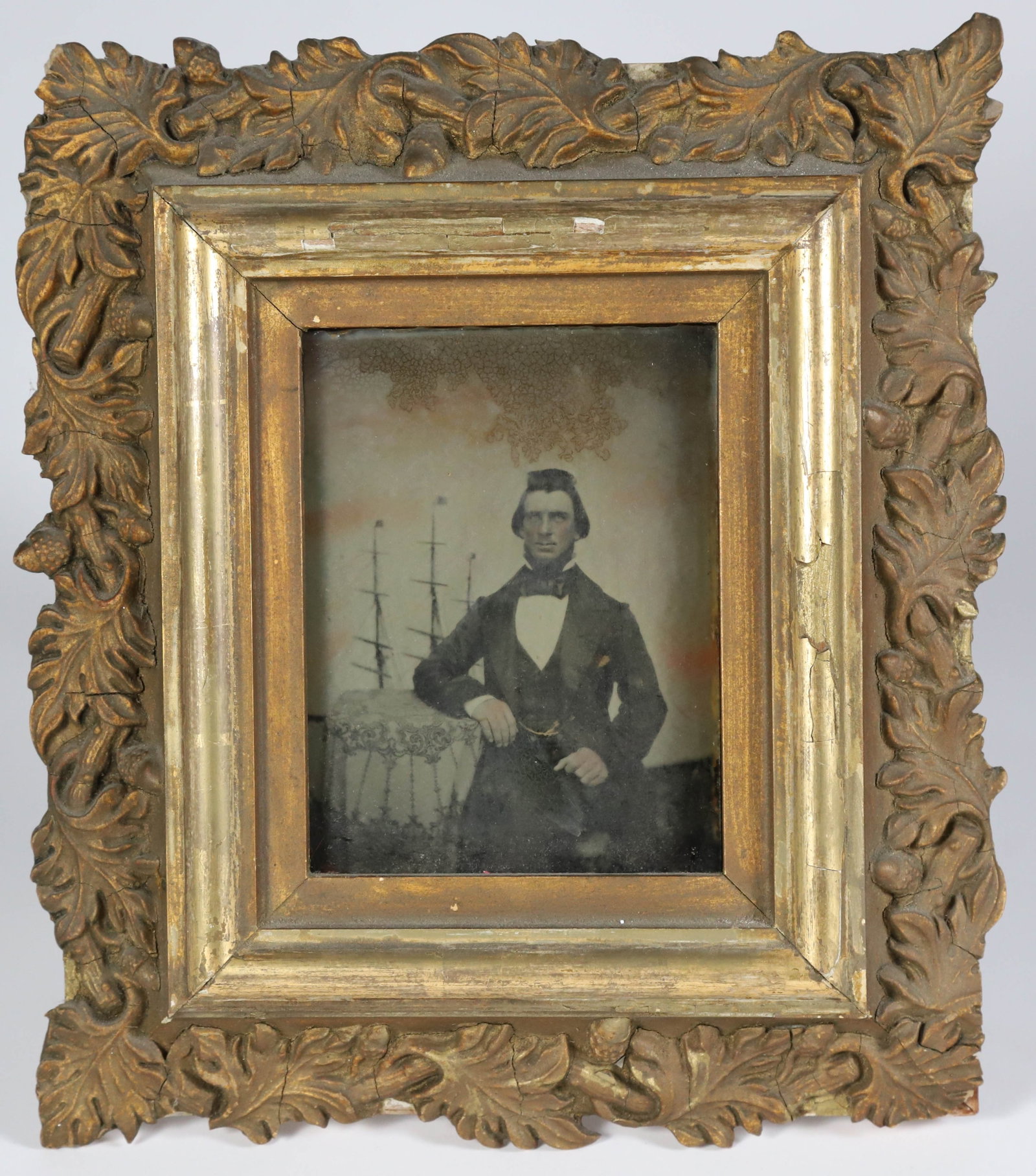 Half Plate Ambrotype of a Nantucket Sea Captain, circa 1857: Half Plate Ambrotype of a Nantucket Sea Captain, circa 1857, with ship masts in the background; in elaborate leaf-carved gilt frame, pencil inscription on reverse: Nantucket, June 10, 1857 Plate: 5.5 