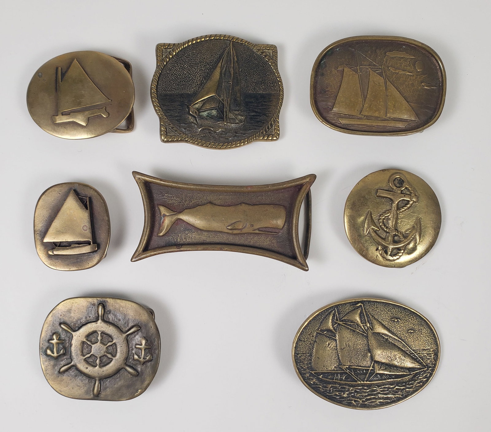 Collection of 8 Vintage American Solid Brass Nautical Belt Buckles, 20th century: Collection of 8 Vintage American Solid Brass Nautical Belt Buckles, 20th century, consisting of sailboats, anchors, ships wheels and Sperm Whale, two marked BTS. 2 in. x 1.75 in. to 2.5 in. x 3.5 in.