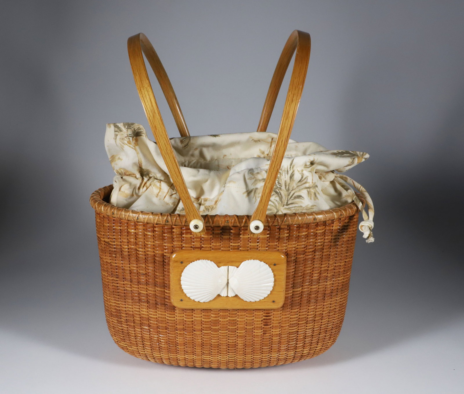 Jean M. Valerio Woven Double Swing Handle Oval Bucket Style Nantucket Basket, circa 1999: Jean M. Valerio Woven Double Swing Handle Oval Bucket Style Nantucket Basket, circa 1999, applied twin carved scallop shells, removable fabric liner, engraved on base Jean M. Valerio 1999 Height 8.5 i