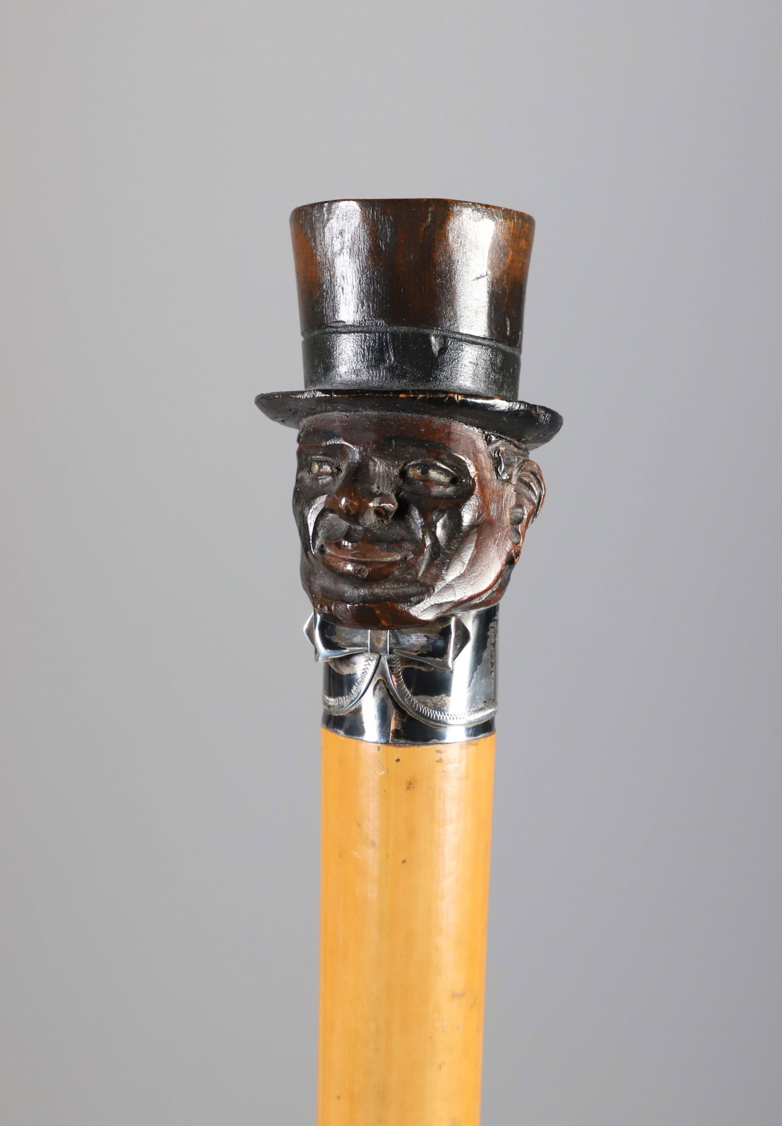 Carved Wood Bust of a Gentleman Walking Stick, 19th Century: Carved Wood Bust of a Gentleman Walking Stick, 19th Century, wearing a top hat and silver bow tie collar, on malacca shaft. Length 37 in. Provenance: The Estate of Herbert E. Sackett, Bristol, Rhode I