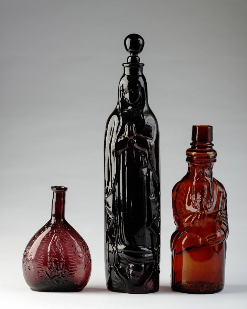 Three Brown Glass Bottles With Figures.: The first, a 'Fac-Simile of first poland water bottle' by Hiram Picker & Sons, height 9 inches. The second, depicting Madonna, height with stopper 14 inches. The third, depicting the virgin Mary, and 