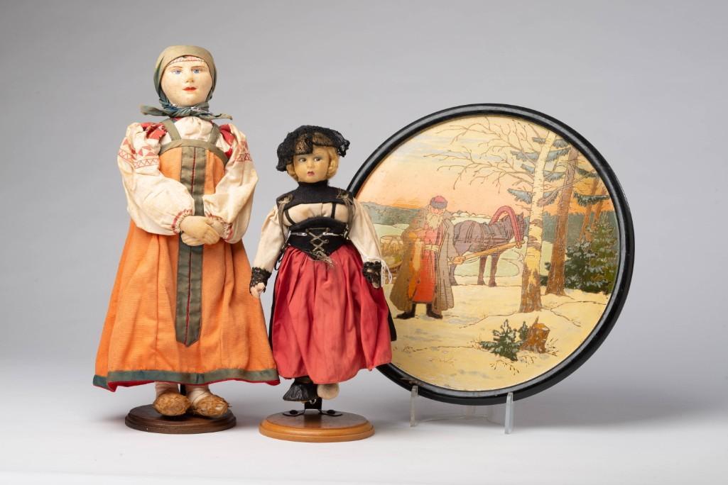 Two Russian Dolls.: With stands, heights 15 and 12 inches. Together with a carved and painted wooden scene of a furrier holding a fox, diameter 12 5/8 inches.