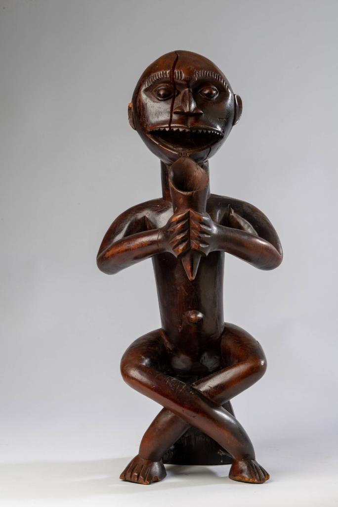 African Carved Wooden Sculpture.: Depicting a man sitting cross legged on a stool, drinking from a cup. Height 23 inches.