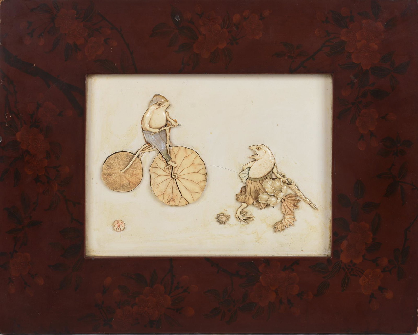 Whimsical Japanese Inlaid Plaque: circa 1900, depicting a frog riding a lotus wheeled bicycle and another dressed in lotus leaves, artist signed with an inlaid plaque lower left and on the back, also has mark for Kuhn and Komor, a Yok