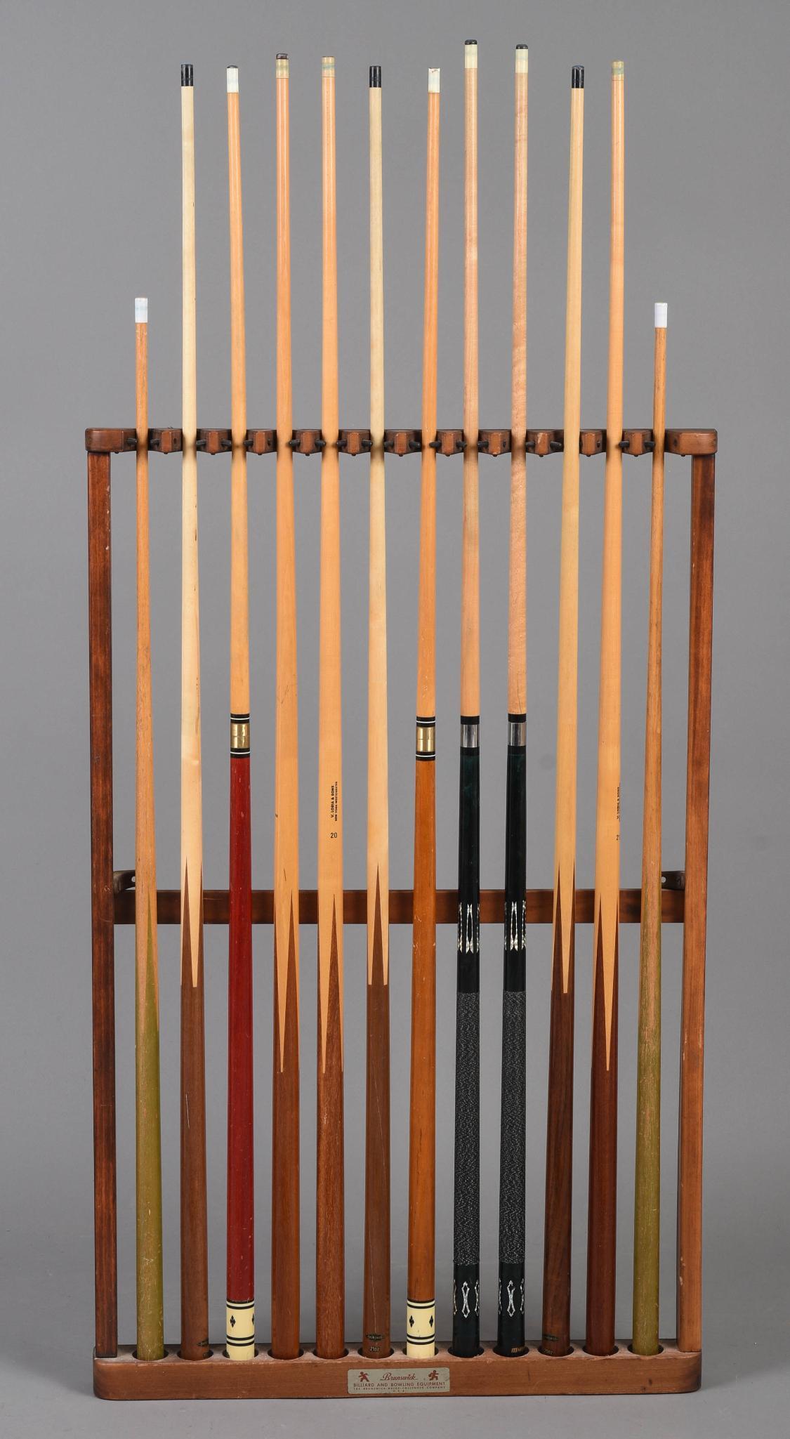 Collection of Pool Cues and a Rack.: The rack by Brunswick Billiard and Bowling Equipment, brands include Harvard, Brunswick Tru-Balance, V. Loria & Sons, several unmarked. Also includes two junior cues.
