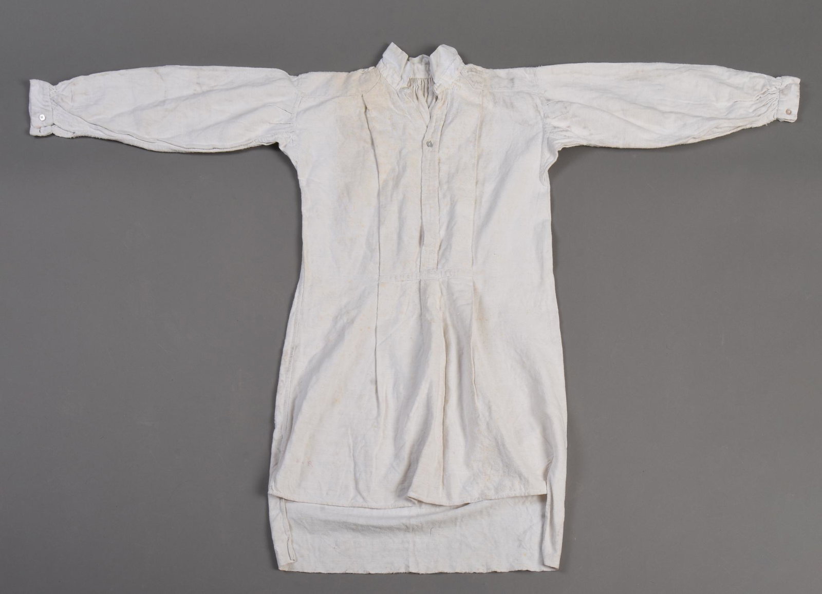 Working Man’s Coarse Linen Shirt, c. 1830: Shirt hand-sewn of relatively coarse, plain-weave, off-white linen, approximately 33 inches long by 26 inches wide in the body, with 19 inch-long, gusseted sleeves gathered into wristbands of 1 ½