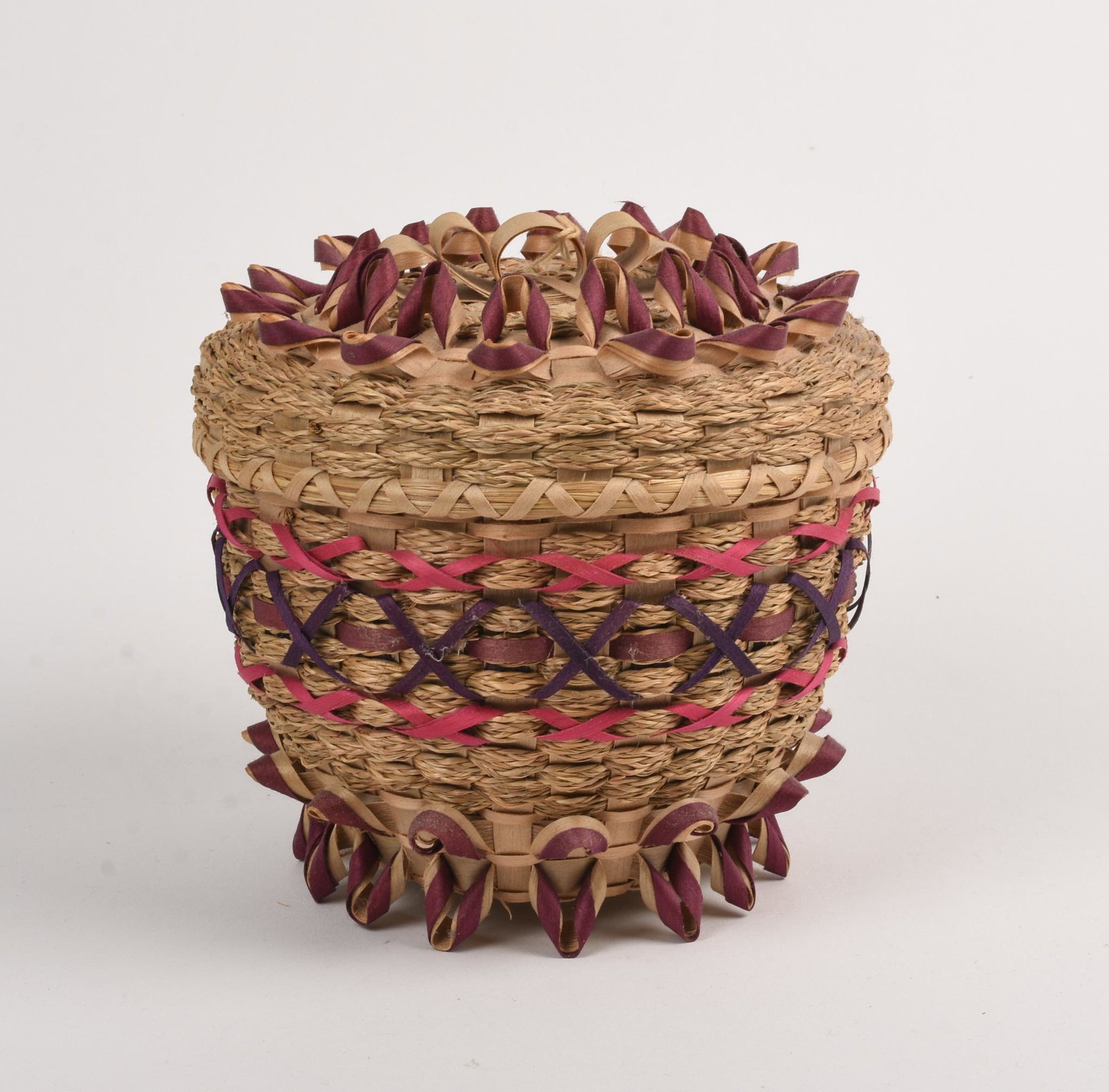 Clara Neptune Keezer Wabanaki Woven Basket.: 1993. Passamaquoddy. Round basket with cover. Maroon and red colors. Height 6 inches, diameter 6.5 inches.