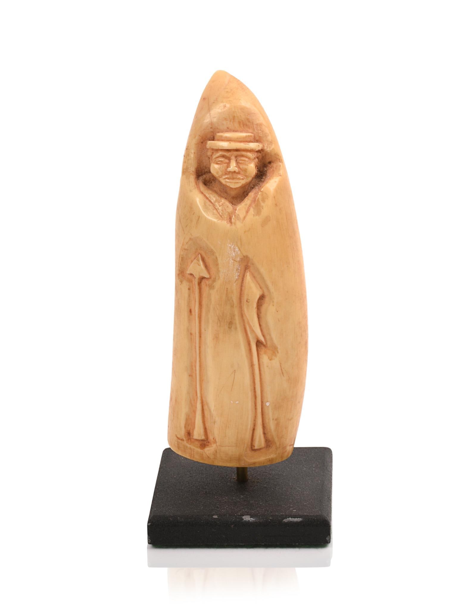 LATE 19TH-EARLY 20TH CENTURY RELIEF-CARVED SPERM WHALE TOOTH: Decorated with a portrait of a whaleman, a killing lance and a harpoon. The back has a highly stylized gent above a sailing sloop. Length: 4.25?. Scrimshaw stand pictured is not part of this lot.