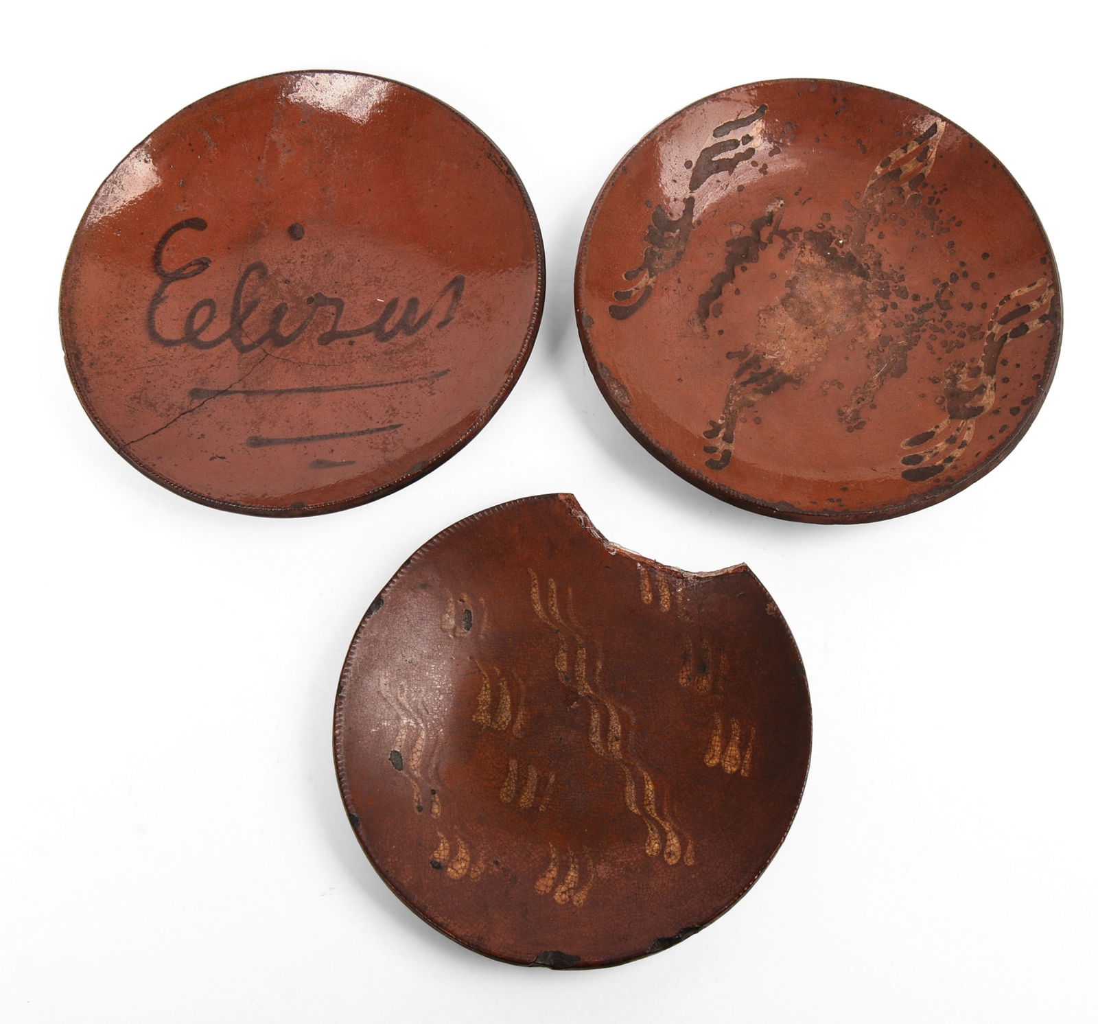 Three Early American Slip Decorated Redware Plates.: Diameters 10 and 11.5 inches. Rim chips to all, loss to smallest plate, one with hairline crack. SHIPPING: We offer very competitively priced in house shipping for all items in this sale. Please conta