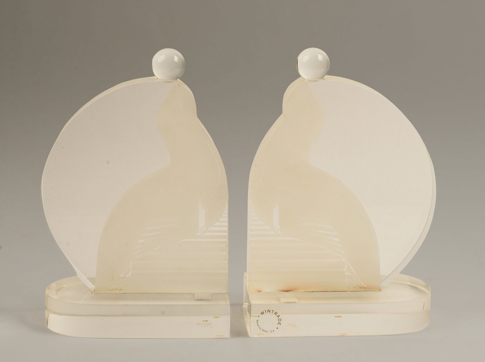 Pair of Acrylic Seal Bookends.: Lucite with frosted seal design balancing a ball, made by Wintrade of Beverly Hills, signed with label. Height 10.5 inches, width 6.5 inches.