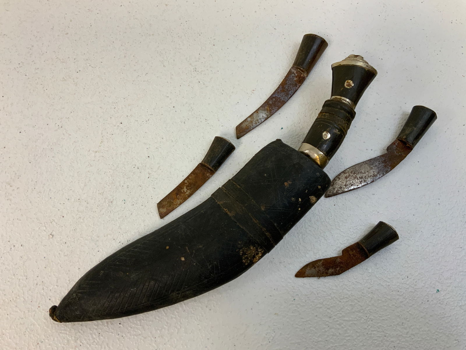 INDIA 5 PIECE GURKHA INDIAN KUKRI KNIFE WITH LEATHER SCABBARD: INDIA 5 PIECE GURKHA INDIAN KUKRI KNIFE WITH LEATHER SCABBARD. SHOWS WEAR AND SOME RUST. COMES WITH 4 SMALL KNIVES. 10" LONG WITH 6" LONG CURVED BLADE ON THE LARGE KNIFE.