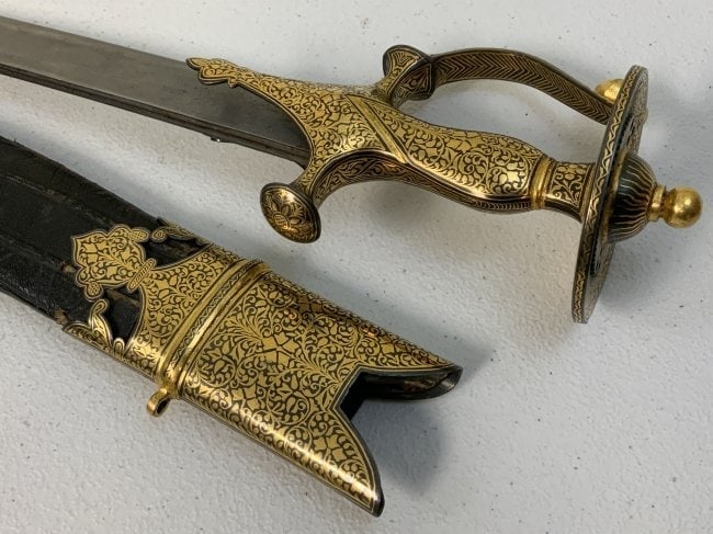 ANTIQUE INDIAN GOLD DECORATED FITTINGS TULWAR SWORD: ANTIQUE INDIAN GOLD DECORATED FITTINGS TULWAR SWORD . BEAUTIFUL PIECE. VERY NICE CONDITION . BEAUTIFUL GOLD DECORATED FITTINGS. NICE STRONG BLADE. OLD PRESSED DECORATED LEATHER ON THE SCABBARD. 37" LO