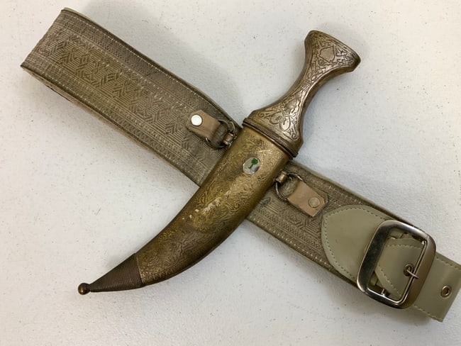 VINTAGE SAUDI ARABIA JAMBIYA DAGGER WITH BELT: SAUDI ARABIA VINTAGE JAMBIYA DAGGER WITH BELT. BROKADE TYPE BELT . COMPLETE WITH ATTACHED JAMBIYA DAGGER WITH SAUDY ARABIA EMBLEM. WE CAN NOT GET THE DAGGER OUT OF SCABBARD POSSIBLE SOLDERED TOGHETER
