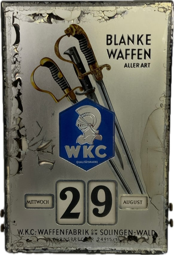 GERMANY THIRD REICH WKC WAFFENFABRIK EDGED WEAPONS MAKER ADVERTISING WALL CALENDAR: WKC Waffenfabrik Advertising Calendar Sign. 14" X 9 1/2" glass plaque mounted on wood box with four windows and four working brass knobs to scroll the month, day, and date, two metal hangers on top. M