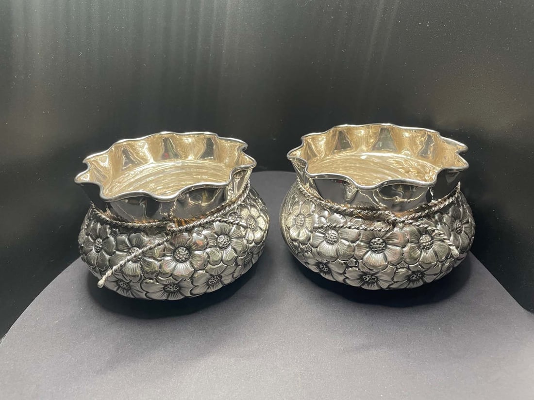 Pr Of 900 SILVER FLORAL REPOUSSE ROPE PINCHED BASKET FORM BOWLS Marked, ''900 A.K'' (on the: Pr Of 900 SILVER FLORAL REPOUSSE ROPE PINCHED BASKET FORM BOWLS Marked, ''900 A.K'' (on the inside), features a ruffled rim basket form pinched by a tied rope near the top. The bulbous body of the bow