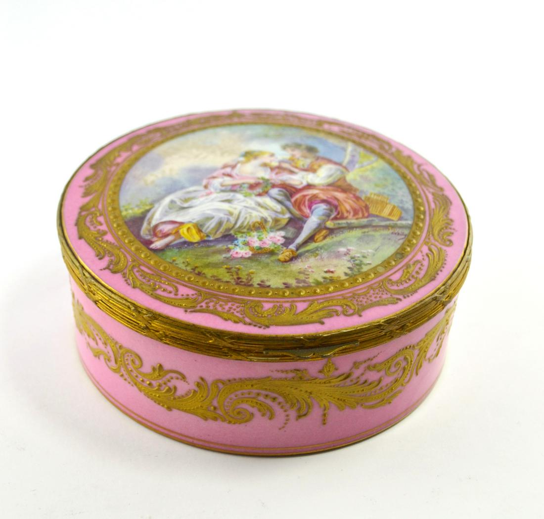 French porcelain box.: Caja redonda en porcelana francesa color rosado con detalles en oro, con montura en bronce y "escena galante" central pintada a mano. Medidas: alto 6 cm - diámetro 14.5 cm.