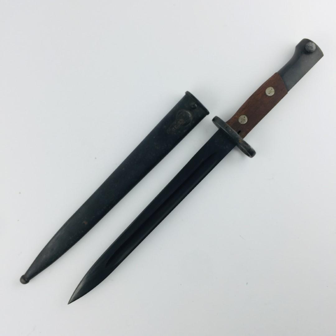 Bayonet: Bayonet for Yugoslavian Mauser model 44 rifle. Wooden handles. Metal scabbard numbered "86919". Bayoneta para fusil Mauser yugoslavo modelo 44. Cachas en madera. Vaina en metal con numeración "86