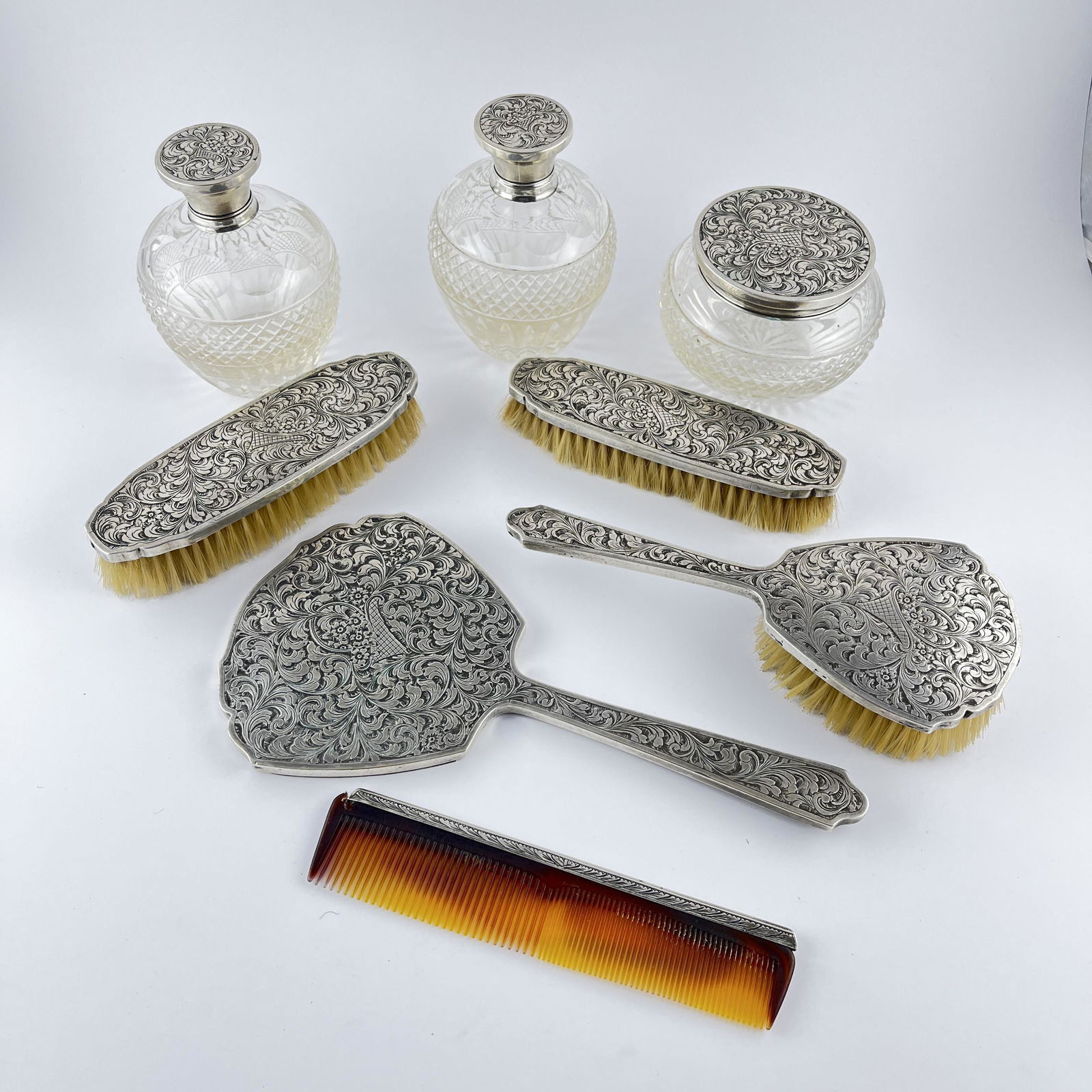 Silver vanity set: Silver 800 engraved "leaves and flowers" dressing table set. Composed of a comb, three brushes, a hand mirror and three flasks with cut glass reservoirs. Juego de tocador en plata 800 cincelada "hojas