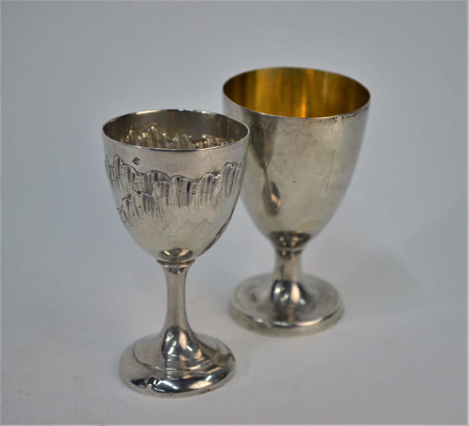 George III silver egg-cup and another: A George III silver egg-cup with gilt interior, on stemmed foot, (probably) Thomas Liddiard, London c.1786/7 (marks rubbed), to/w a French .950 grade egg-cup with embossed and chased rocaille-work (2)