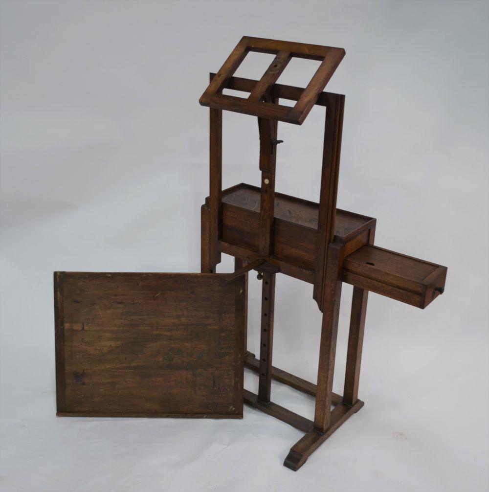 An antique oak artist's easel/table: An antique oak artist's easel/table with rise and tilt mechanism, box drawer to end, raised on square frame, bears retailers ivorine disc for G Roberson & Co Ltd London, 65 x 50 x 75 cm high