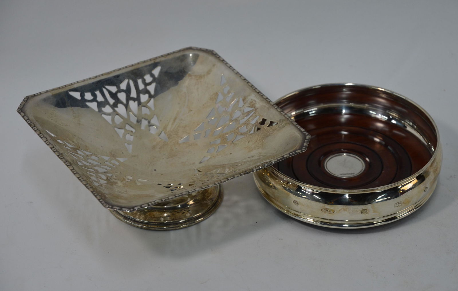 A silver bottle coaster and a pierced silver square: A silver bottle coaster with turned wood base, Sheffield 2000, to/w a pierced silver square comport on moulded foot, Birmingham 1930, 4 oz (2)