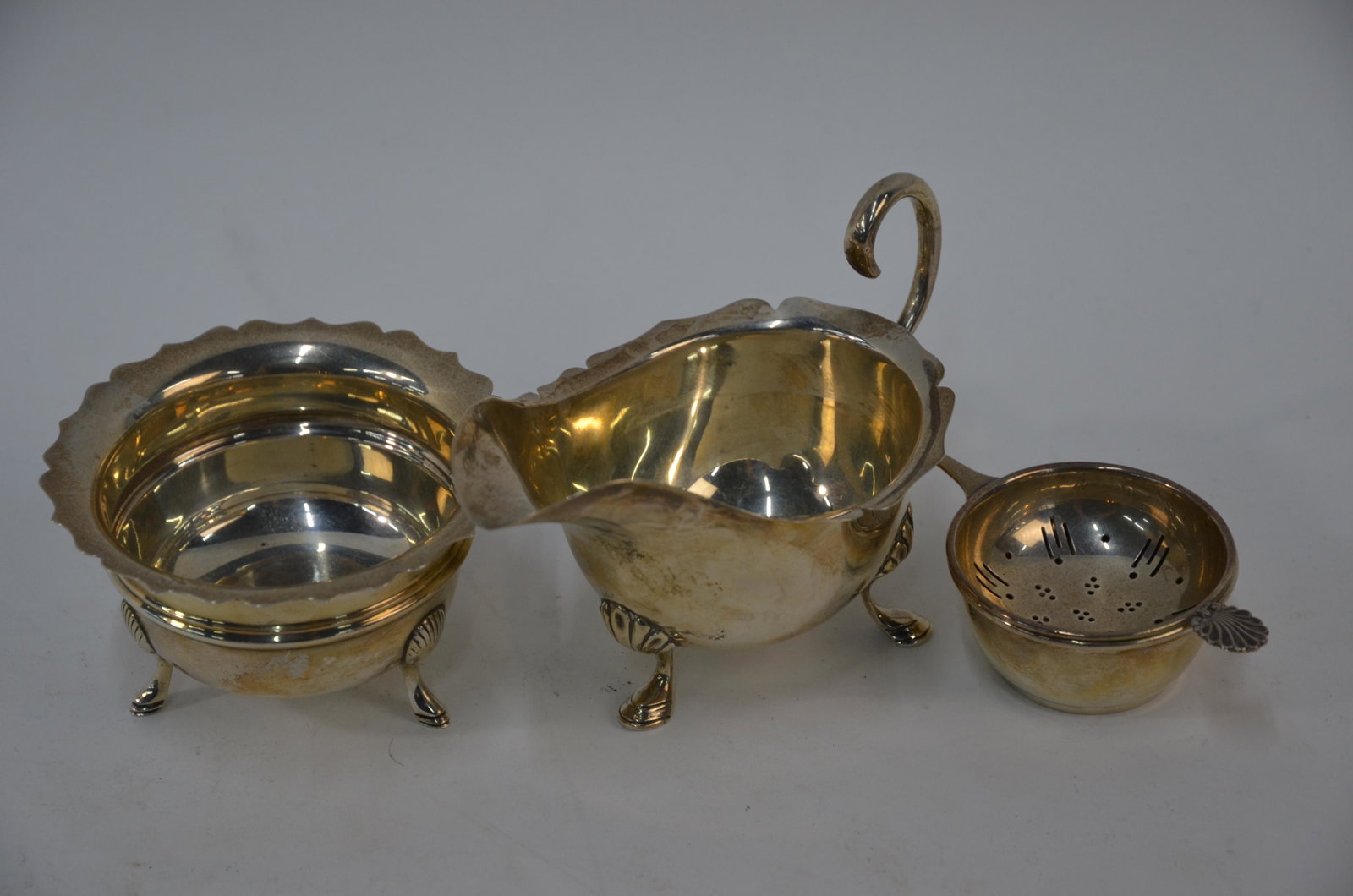 An Edwardian silver cream jug, sugar bowl and tea: An Edwardian silver cream jug and similar sugar bowl, on hoof feet, Birmingham 1907 to/w a tea strainer on stand, Birmingham 1970 (3) 6.8 oz