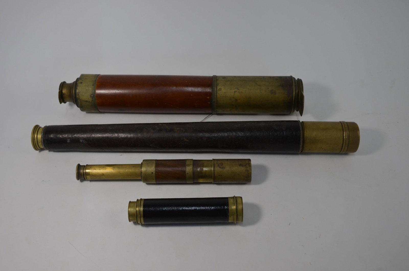 Four telescopes: A Victorian brass three-drawer telescope with teak sleeve, Geo. Willis Hinchliffe's Celebrated, 102 cm o/a, to/w another telescope with leather sleeve, by Dobbie McInnes & Clyde Ltd, 69 cm long, a fou