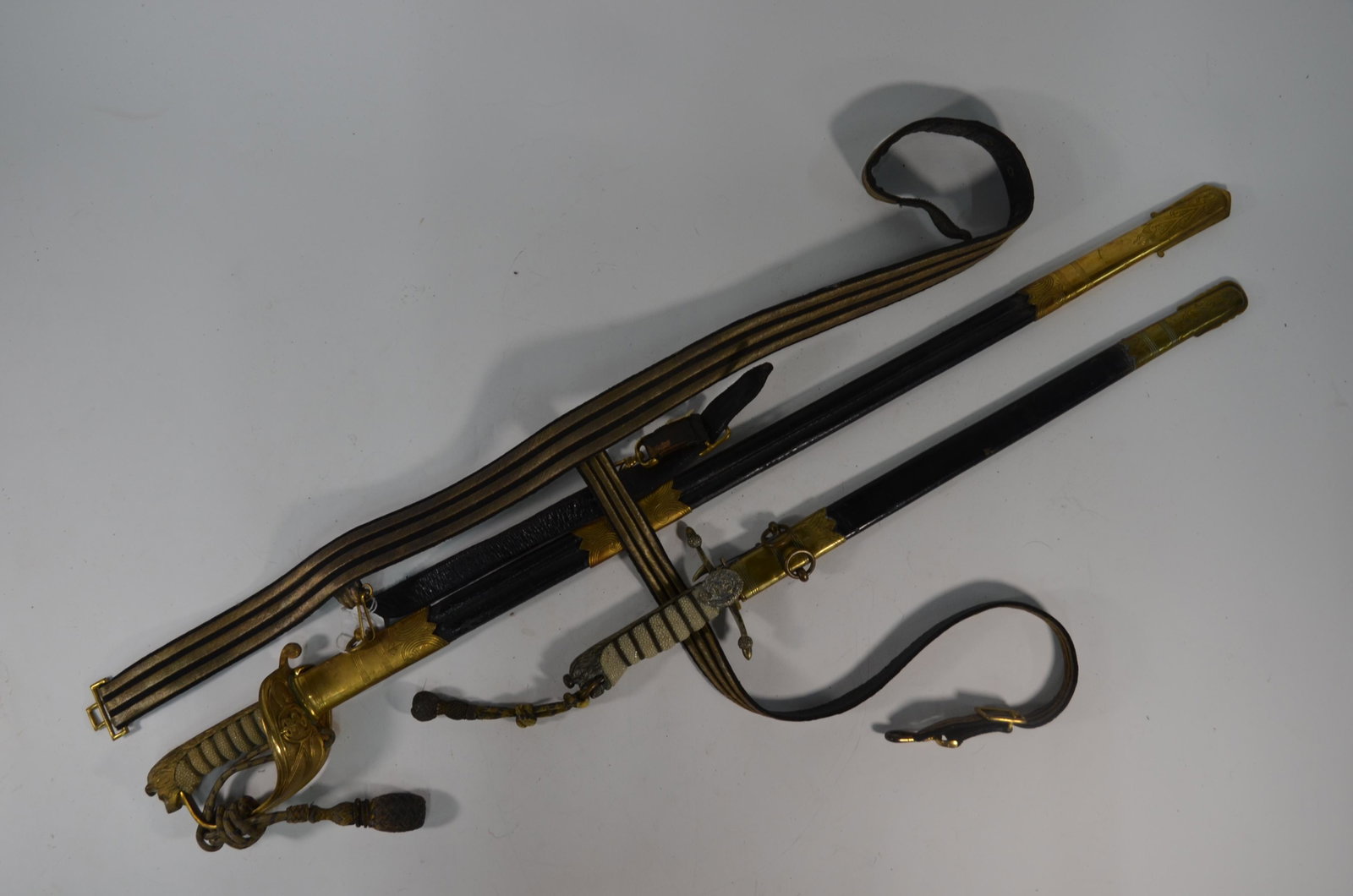 A Naval Officer's sword by Gieves: A Naval Officer's sword by Gieves, with etched 80 cm blade, gilt brass basket hilt with wired shagreen grip, lion's head pommel and bullion knot, in brass-mounted leather scabbard, 95 cm long overall,