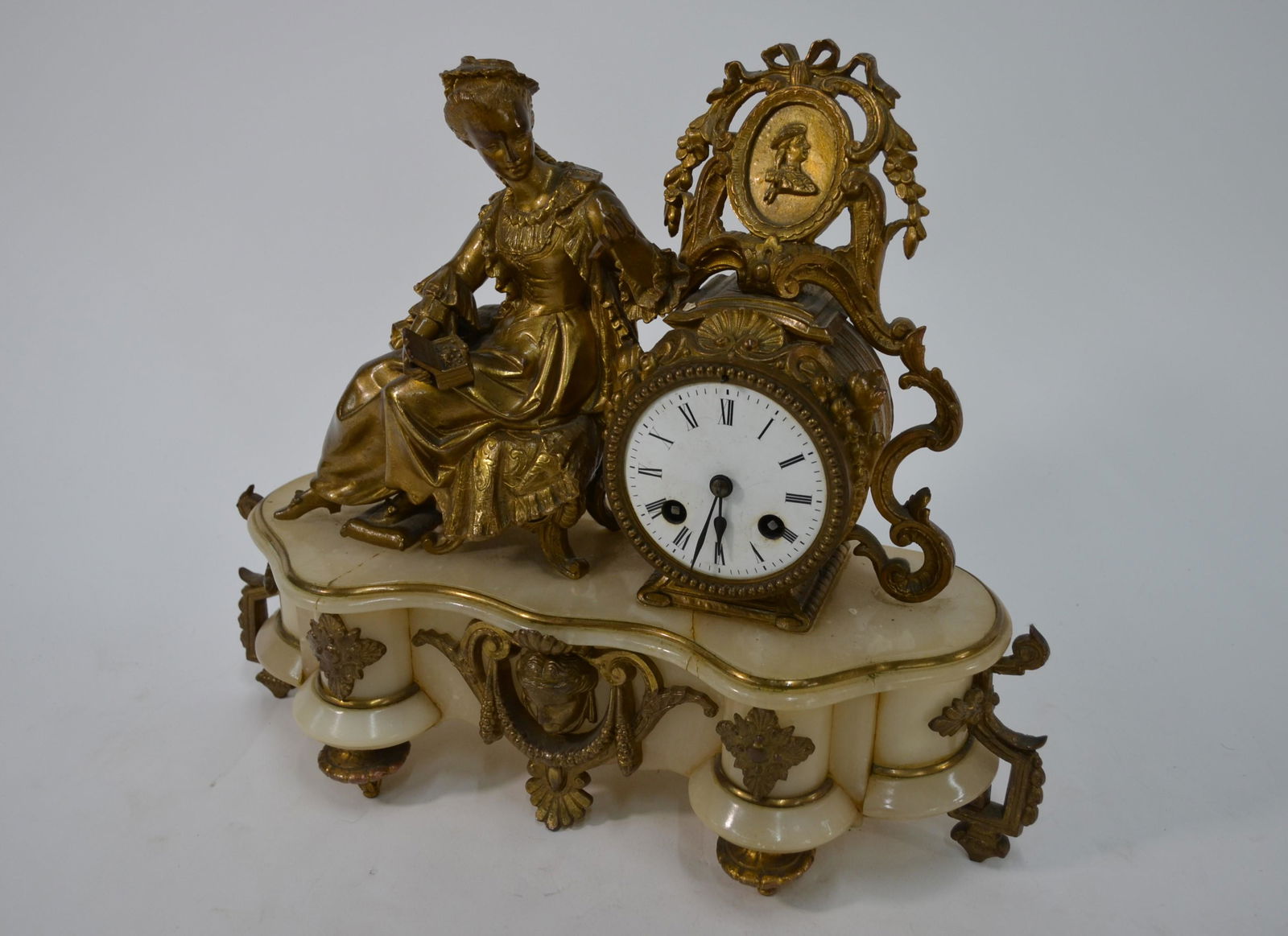 A late 19th century gilt-metal mounted alabaster drum: A late 19th century gilt-metal mounted alabaster drum mantel clock, the two train French movement with white enamelled dial, flanked by a seated lady 31 cm high overall