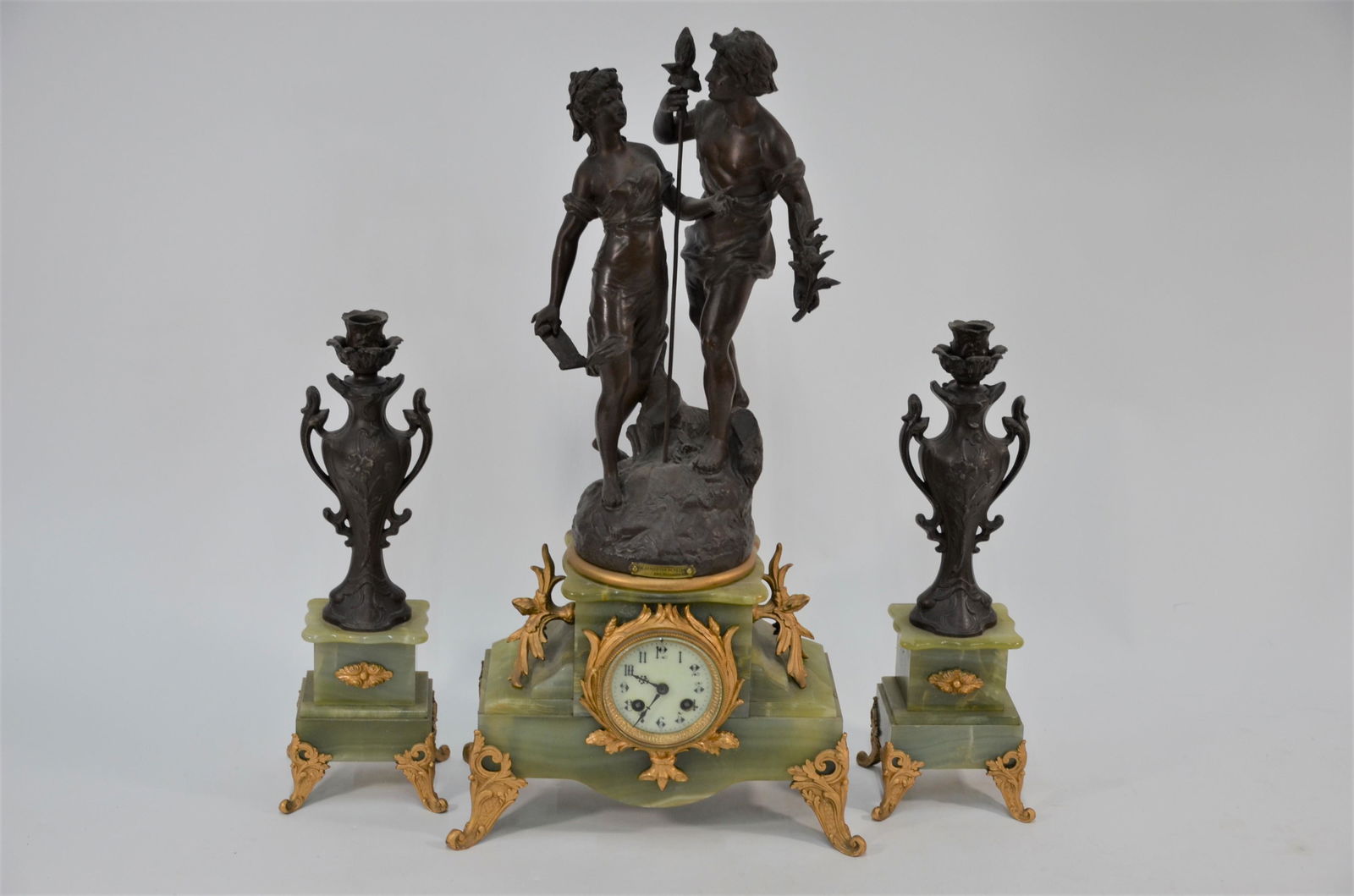 A late 19th/20th century green onyx spelter figural: A late 19th/20th century green onyx spelter figural three piece clock garniture, with two train drum movement striking ona bell, surmounted by a pair of classical figures 'La Recontre du Patre' aftre