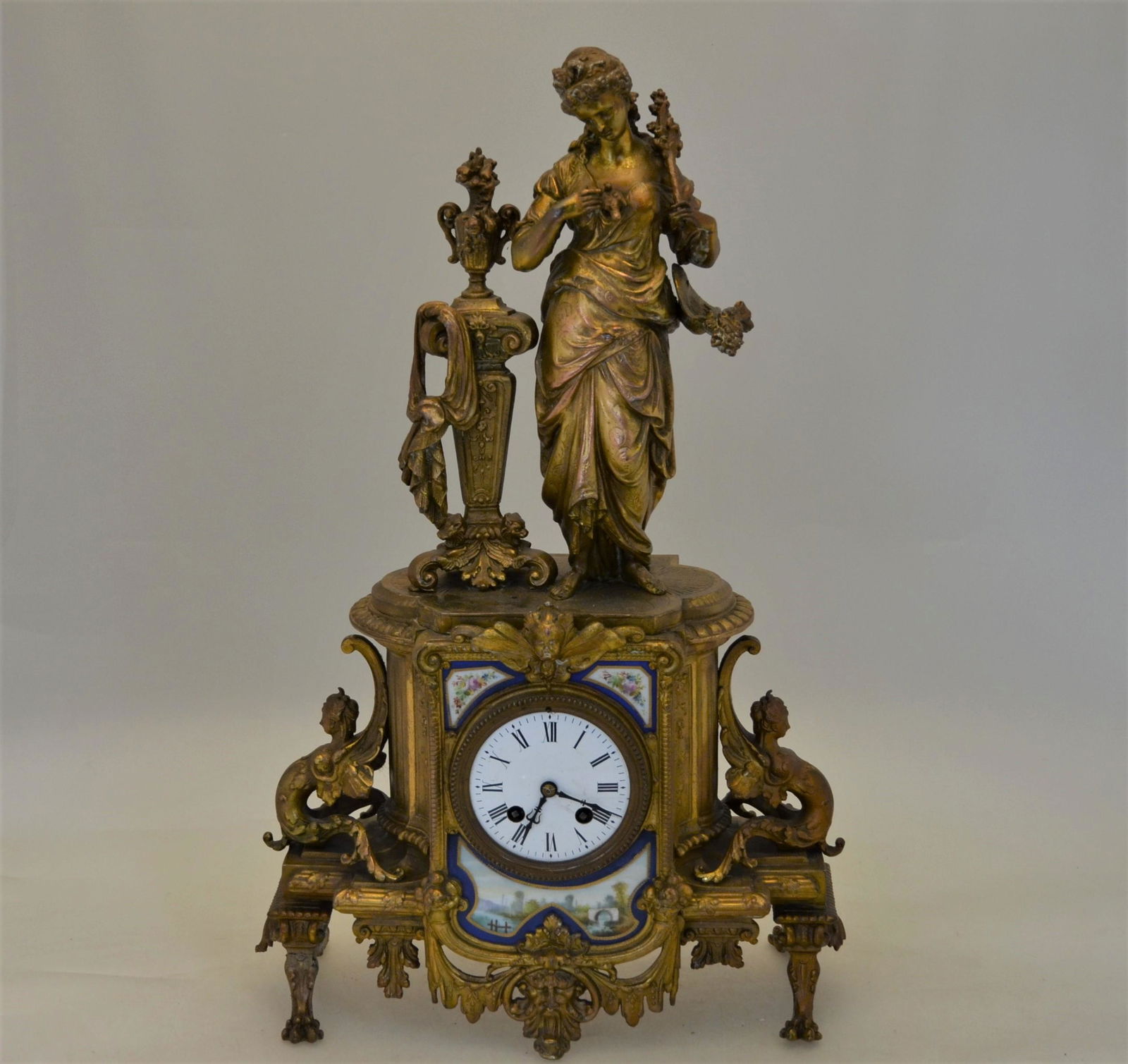 A late 19th century French gilt spelter mantel clock: A late 19th century French gilt spelter mantel clock, the eight day two train drum movement flanked with enamelled porcelain plaque, the case surmounted by a classical female figure, striking the half